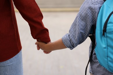 Photo of Mother holding hands with her son and taking him to school outdoors, closeup