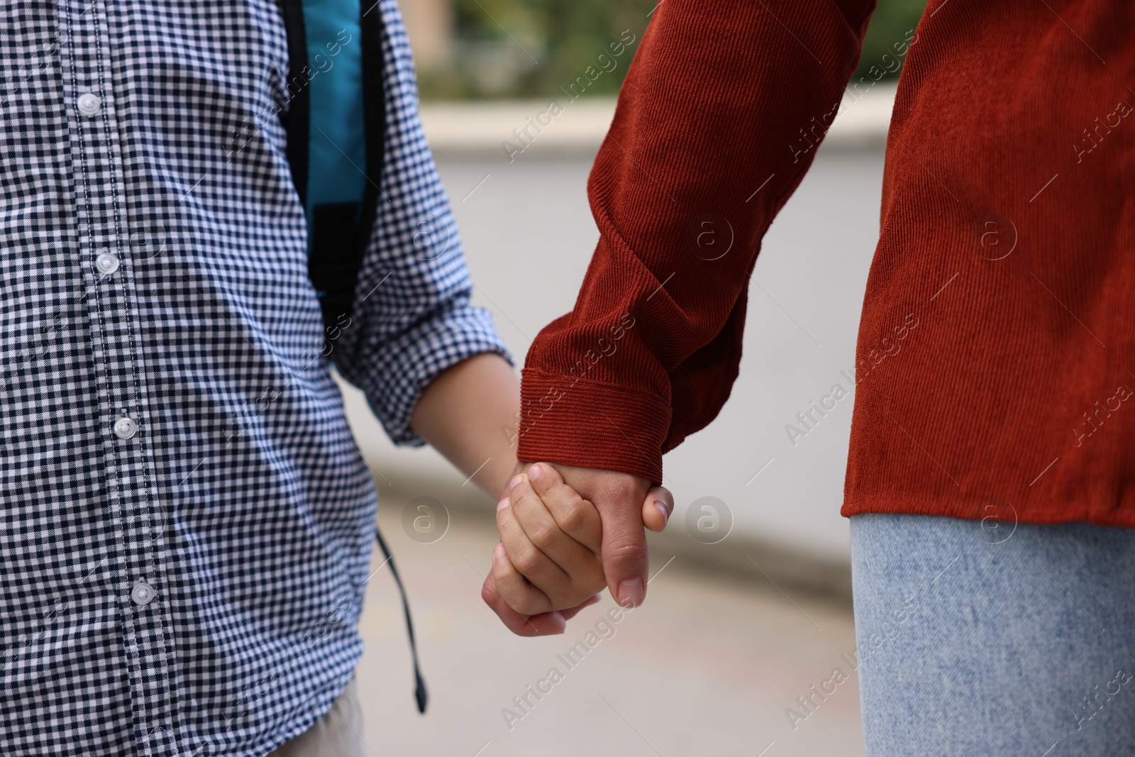 Photo of Mother holding hands with her son and taking him to school outdoors, closeup