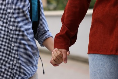 Photo of Mother holding hands with her son and taking him to school outdoors, closeup