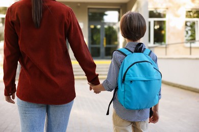 Photo of Mother taking her son to school outdoors, back view