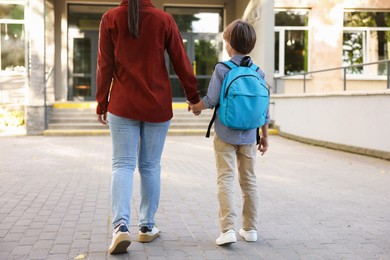 Photo of Mother taking her son to school outdoors, back view