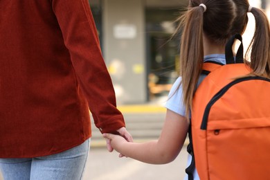 Photo of Mother holding hands with her daughter and taking her to school outdoors, closeup