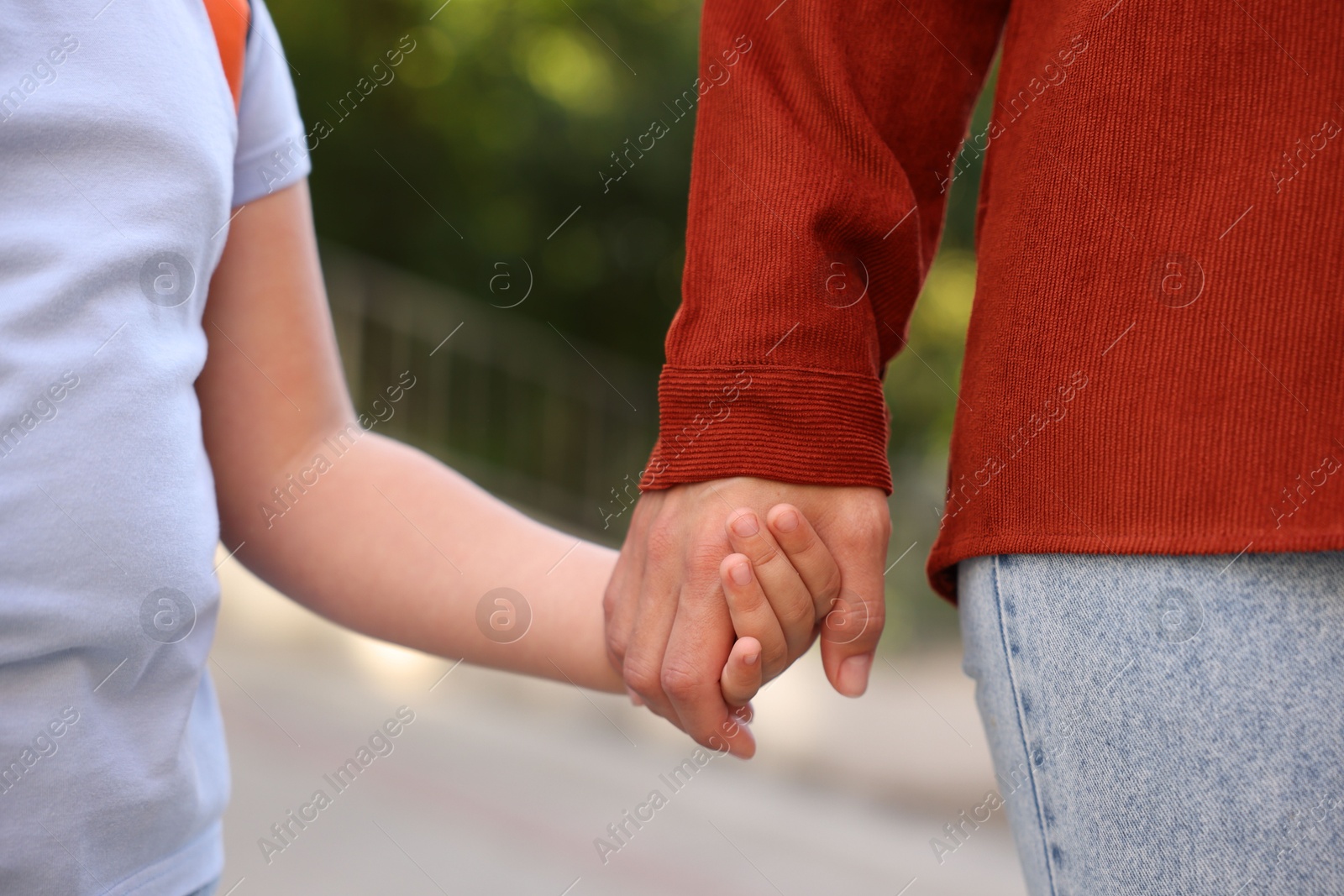 Photo of Mother holding hands with her daughter and taking her to school outdoors, closeup