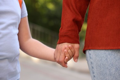 Photo of Mother holding hands with her daughter and taking her to school outdoors, closeup