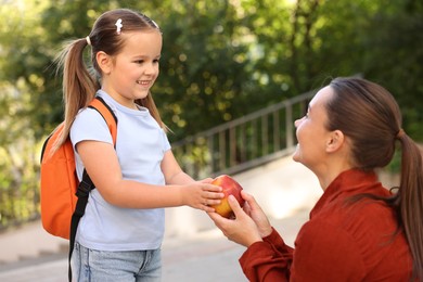 Photo of Mother giving apple to her daughter while taking to school outdoors