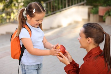 Photo of Mother giving apple to her daughter while taking to school outdoors