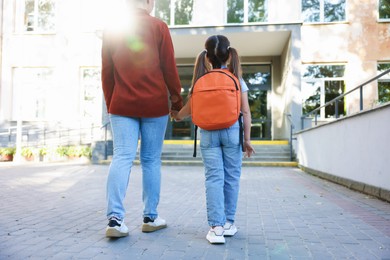 Photo of Mother taking her daughter to school outdoors, back view