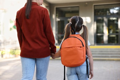 Photo of Mother taking her daughter to school outdoors, back view