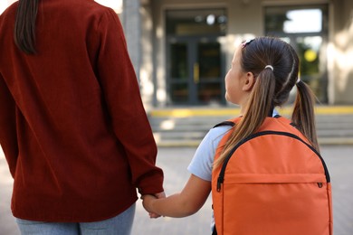Photo of Mother taking her daughter to school outdoors, back view