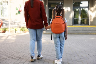 Photo of Mother taking her daughter to school outdoors, back view