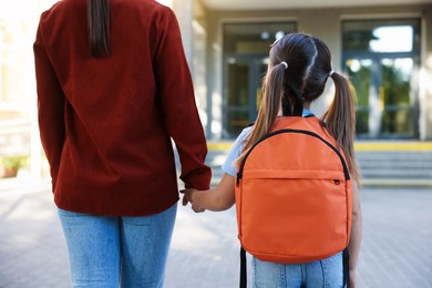 Photo of Mother taking her daughter to school outdoors, back view