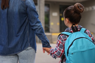 Photo of Mother taking her daughter to school outdoors, back view