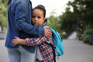 Photo of Mother hugging her daughter while taking her to school outdoors, closeup. Space for text