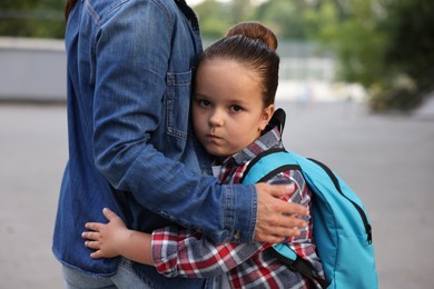 Photo of Mother hugging her daughter while taking her to school outdoors, closeup