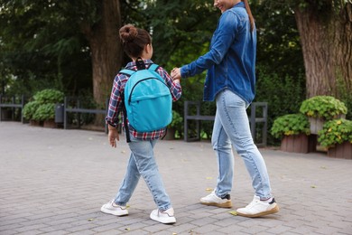Photo of Mother taking her daughter to school outdoors, back view