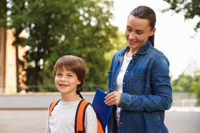 Photo of Mother putting book into son's backpack while taking him to school outdoors