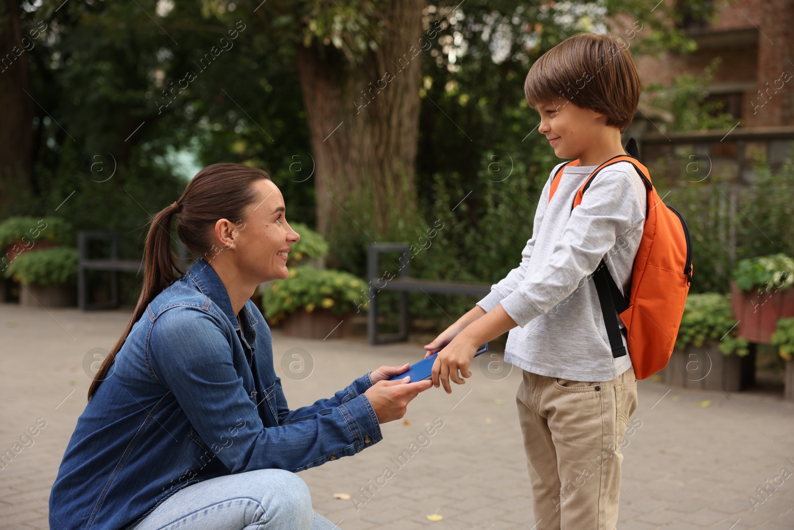 Mother giving book to her son while taking him to school outdoors Photo of Mother giving book to her son while taking him to school outdoors