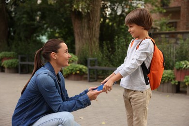 Photo of Mother giving book to her son while taking him to school outdoors