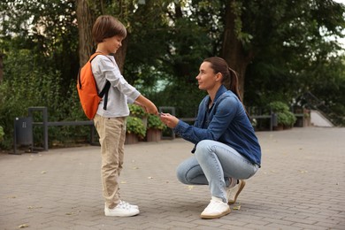 Photo of Mother giving book to her son while taking him to school outdoors