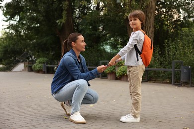 Photo of Mother giving book to her son while taking him to school outdoors