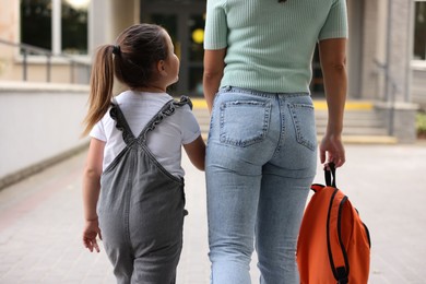 Photo of Mother taking her daughter to school outdoors, back view