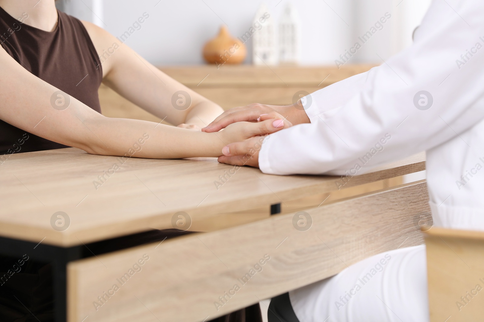 Doctor checking woman's pulse with fingers at wooden table indoors, closeup Photo of Doctor checking woman's pulse with fingers at wooden table indoors, closeup