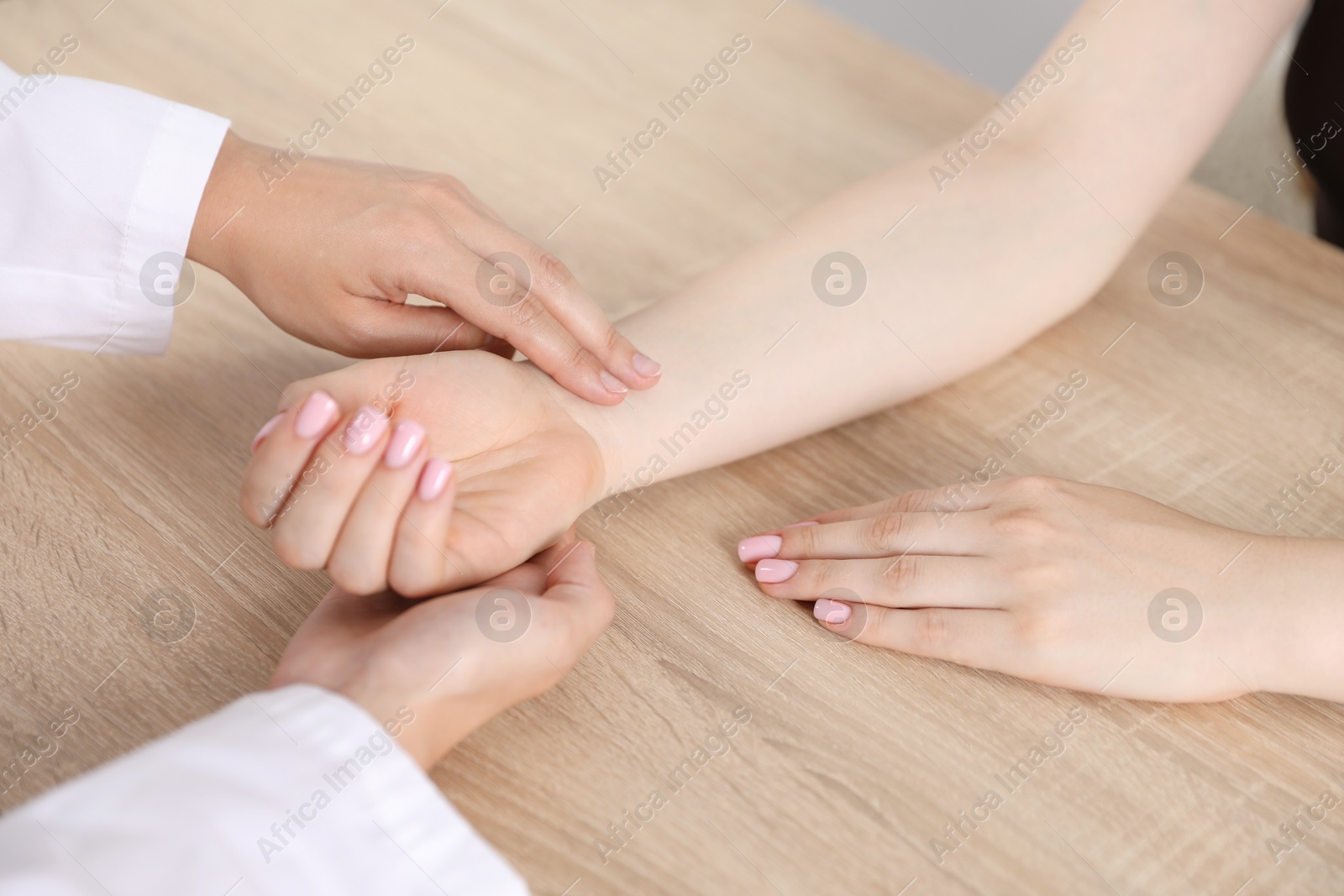 Doctor checking woman's pulse with fingers at wooden table indoors, closeup Photo of Doctor checking woman's pulse with fingers at wooden table indoors, closeup