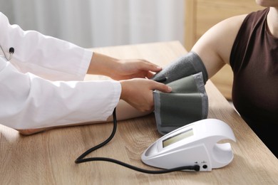 Photo of Doctor checking woman's heart rate and blood pressure via sphygmomanometer at wooden table indoors, closeup