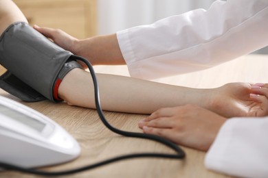 Photo of Doctor checking woman's heart rate and blood pressure via sphygmomanometer at wooden table indoors, closeup