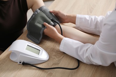 Photo of Doctor checking woman's heart rate and blood pressure via sphygmomanometer at wooden table indoors, closeup
