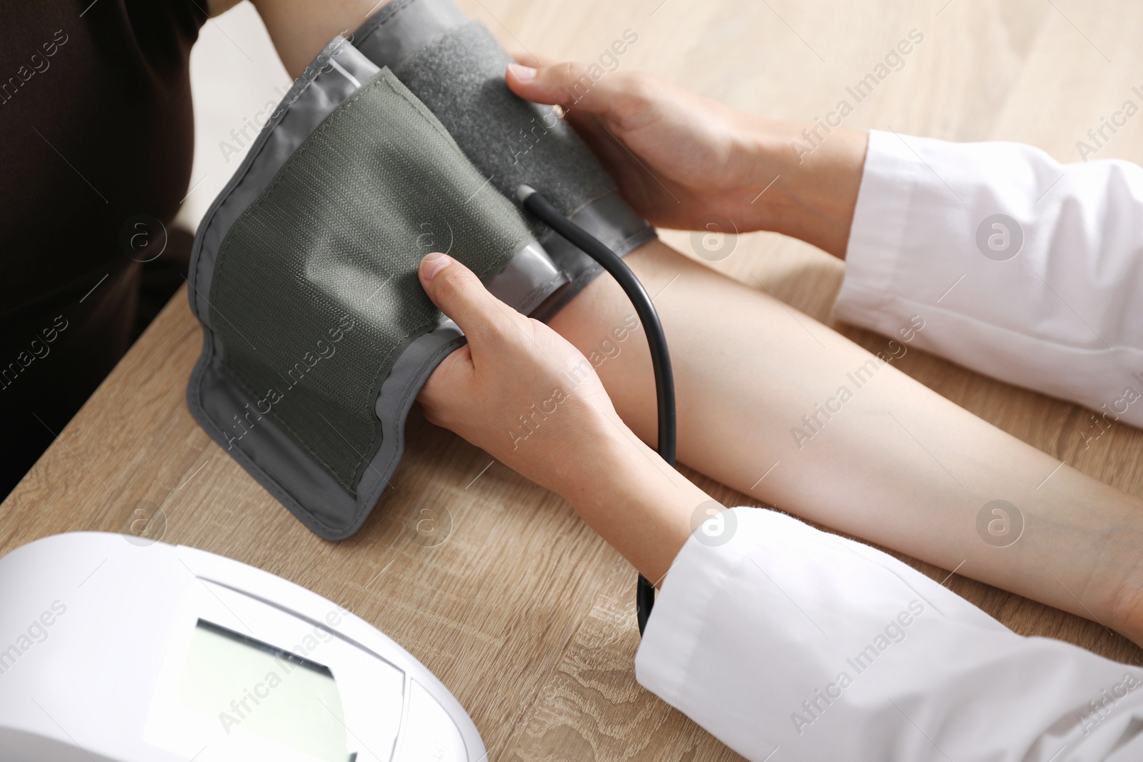 Photo of Doctor checking woman's heart rate and blood pressure via sphygmomanometer at wooden table indoors, closeup