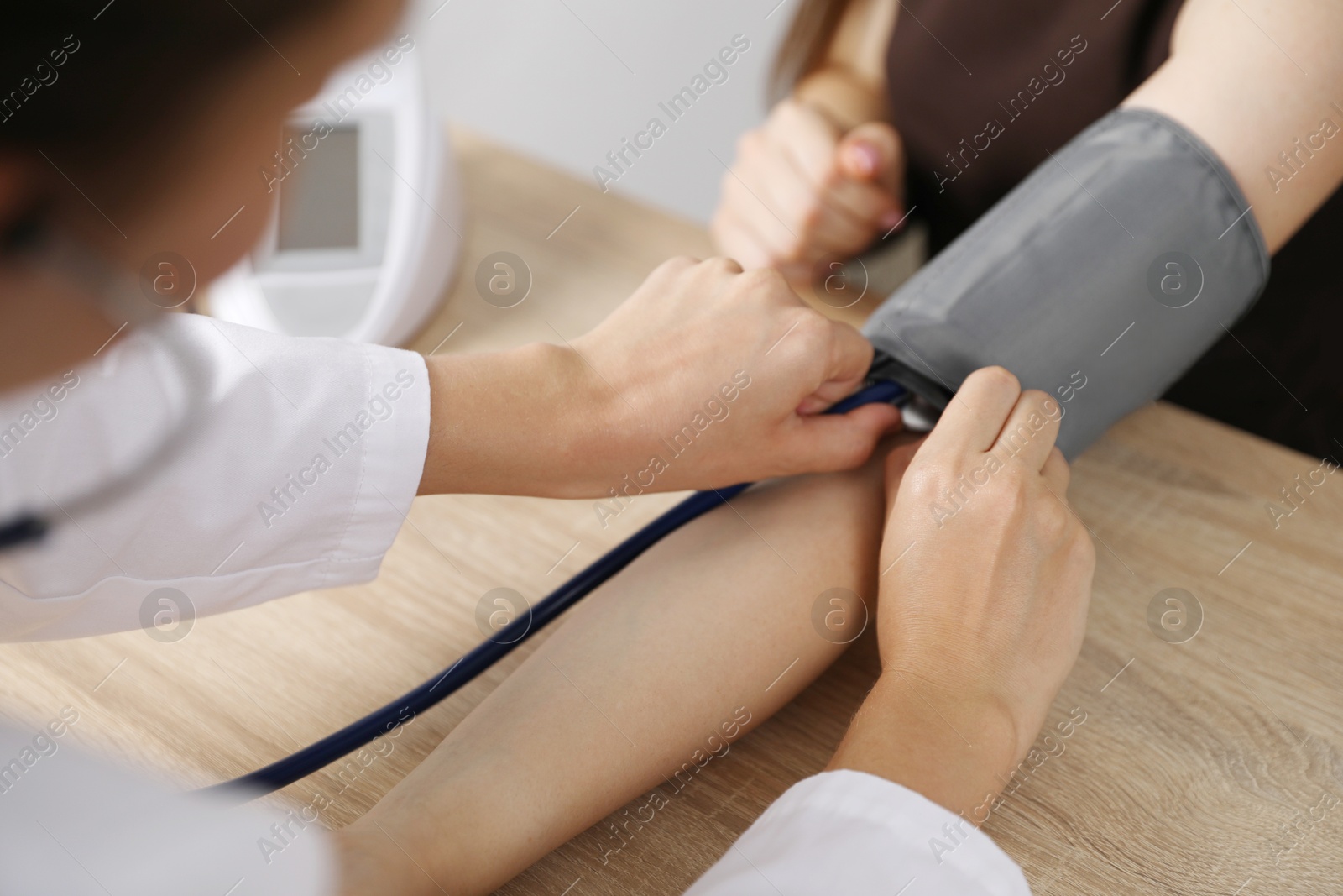 Doctor checking woman's heart rate and blood pressure via sphygmomanometer at wooden table indoors, closeup Photo of Doctor checking woman's heart rate and blood pressure via sphygmomanometer at wooden table indoors, closeup