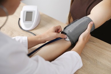 Photo of Doctor checking woman's heart rate and blood pressure via sphygmomanometer at wooden table indoors, closeup