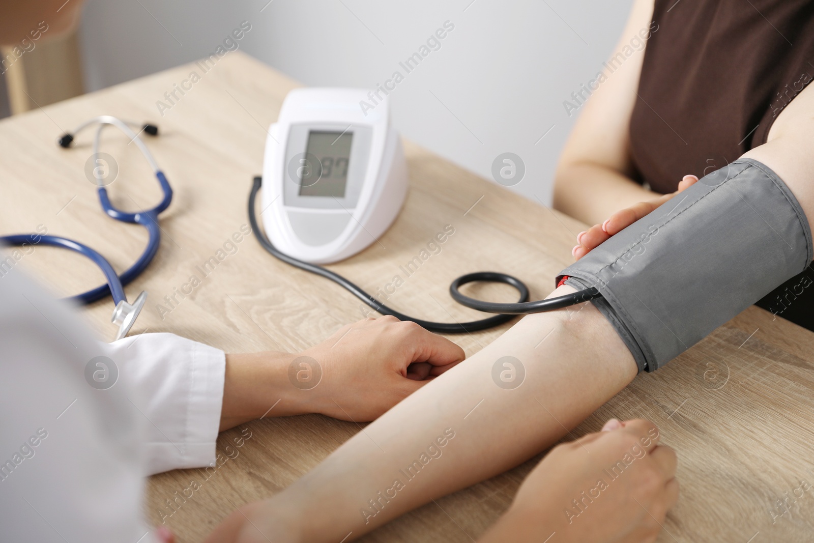 Doctor checking woman's heart rate and blood pressure via sphygmomanometer at wooden table indoors, closeup Photo of Doctor checking woman's heart rate and blood pressure via sphygmomanometer at wooden table indoors, closeup