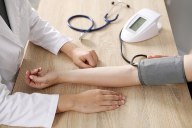 Photo of Doctor checking woman's heart rate and blood pressure via sphygmomanometer at wooden table indoors, closeup