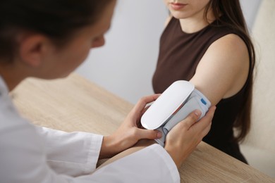 Photo of Doctor checking woman's heart rate and blood pressure via sphygmomanometer at wooden table indoors, closeup