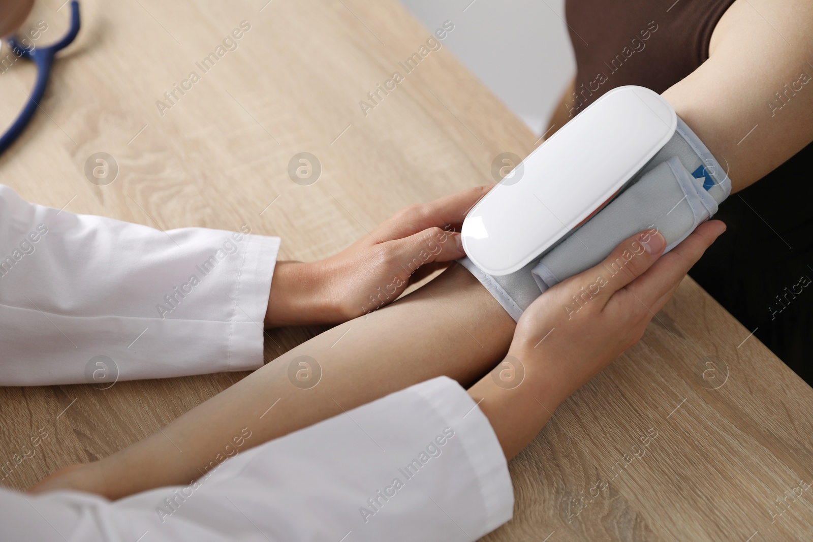 Doctor checking woman's heart rate and blood pressure via sphygmomanometer at wooden table indoors, closeup Photo of Doctor checking woman's heart rate and blood pressure via sphygmomanometer at wooden table indoors, closeup