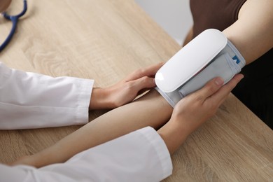 Photo of Doctor checking woman's heart rate and blood pressure via sphygmomanometer at wooden table indoors, closeup