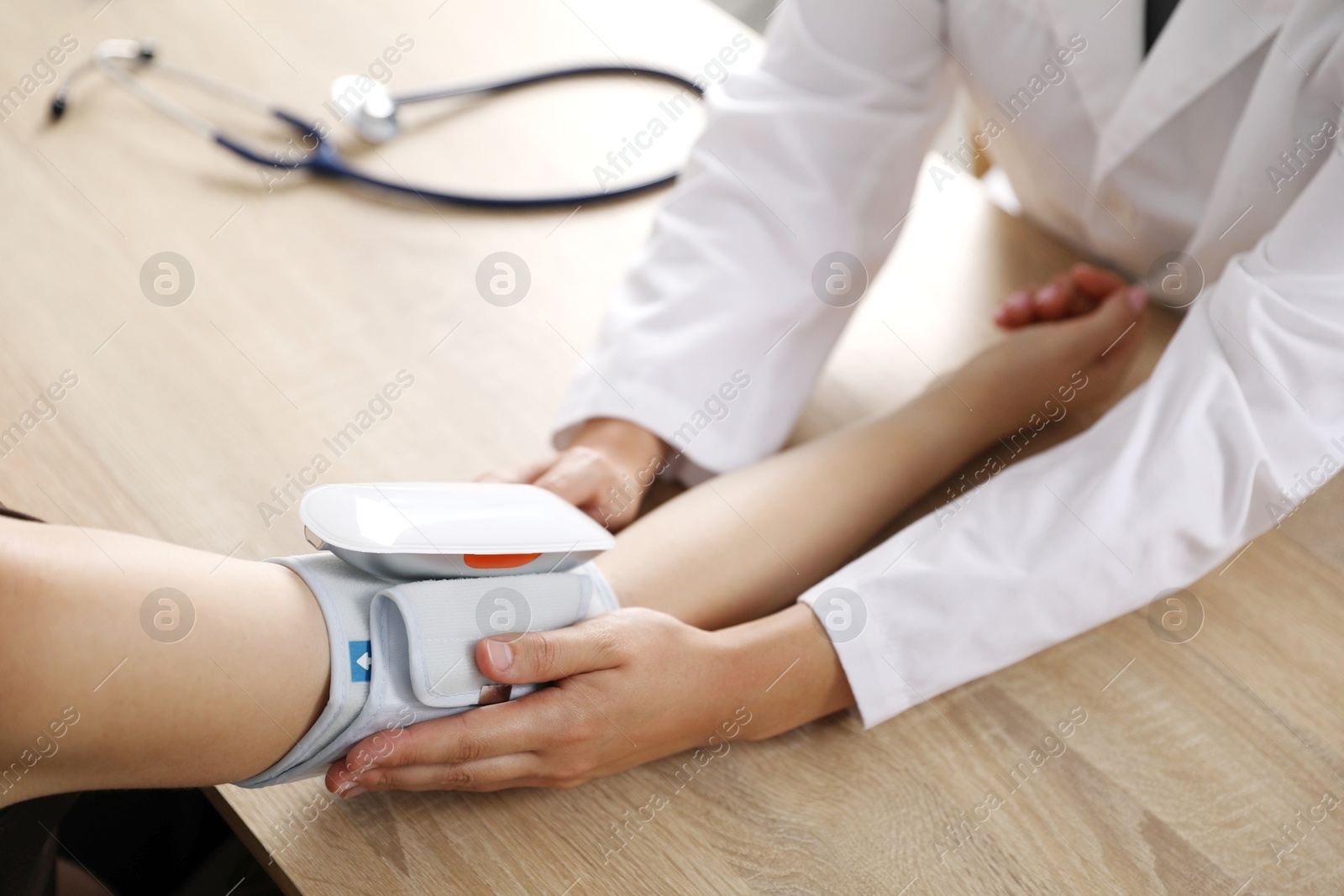 Doctor checking woman's heart rate and blood pressure via sphygmomanometer at wooden table indoors, closeup Photo of Doctor checking woman's heart rate and blood pressure via sphygmomanometer at wooden table indoors, closeup
