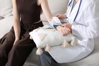 Photo of Doctor checking woman's heart rate and blood pressure via sphygmomanometer on sofa indoors, closeup