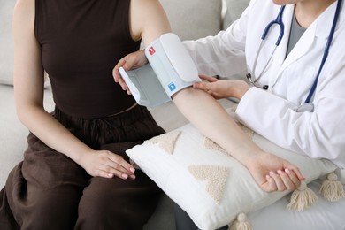 Photo of Doctor checking woman's heart rate and blood pressure via sphygmomanometer on sofa indoors, closeup