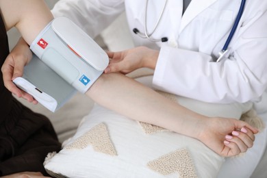 Photo of Doctor checking woman's heart rate and blood pressure via sphygmomanometer on sofa indoors, closeup