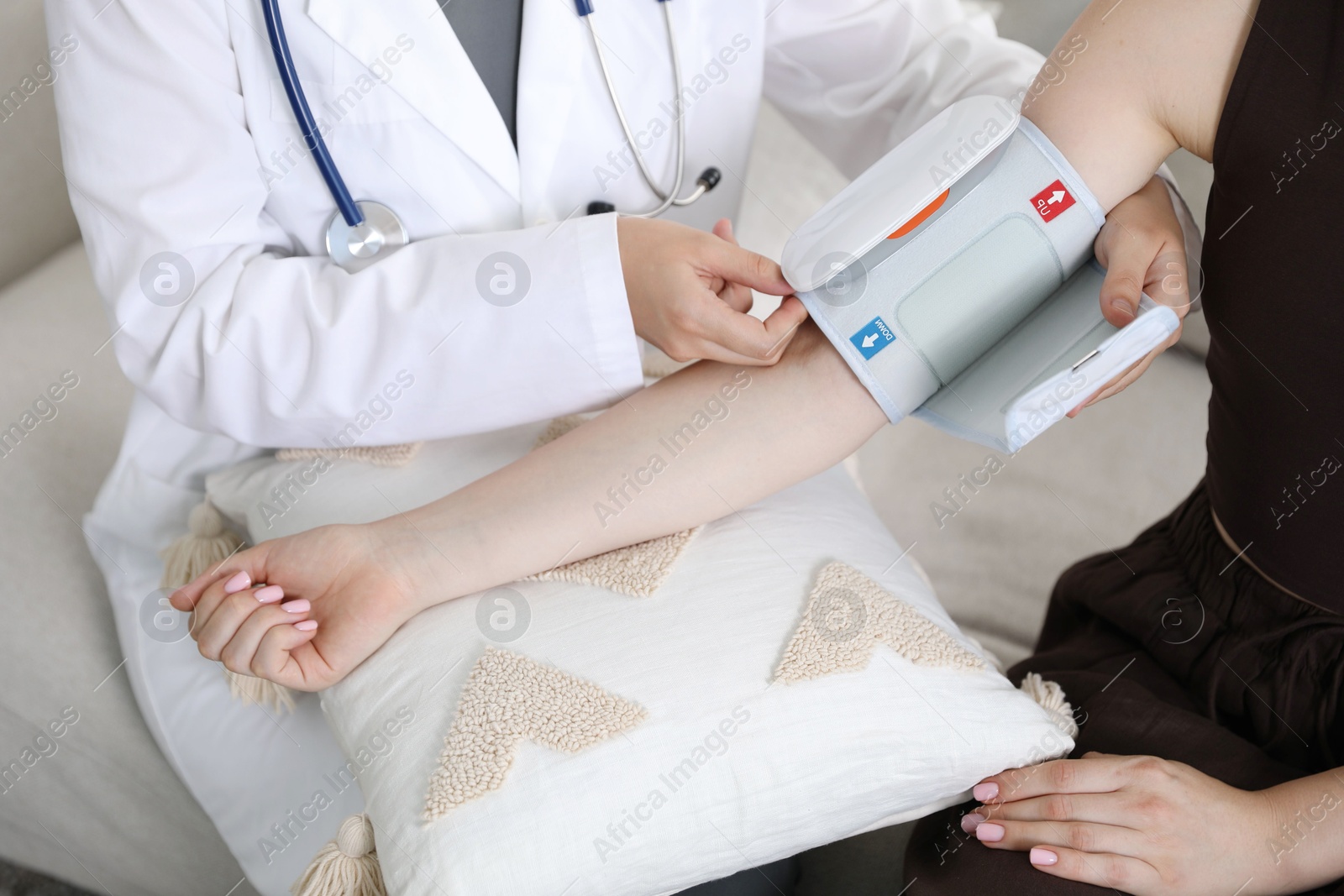 Doctor checking woman's heart rate and blood pressure via sphygmomanometer on sofa indoors, closeup Photo of Doctor checking woman's heart rate and blood pressure via sphygmomanometer on sofa indoors, closeup
