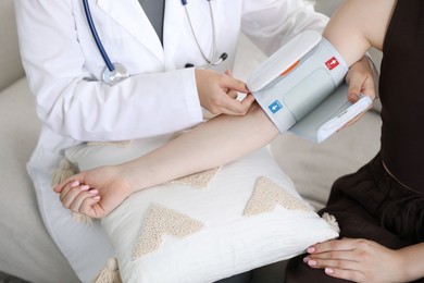 Photo of Doctor checking woman's heart rate and blood pressure via sphygmomanometer on sofa indoors, closeup