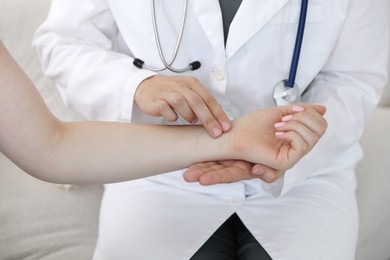 Photo of Doctor checking woman's pulse with fingers indoors, closeup