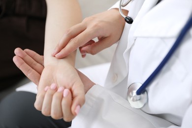 Photo of Doctor checking woman's pulse with fingers indoors, closeup