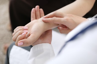 Photo of Doctor checking woman's pulse with fingers indoors, closeup