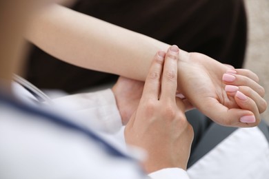Photo of Doctor checking woman's pulse with fingers indoors, closeup