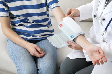 Photo of Doctor checking woman's heart rate and blood pressure via sphygmomanometer on sofa indoors, closeup