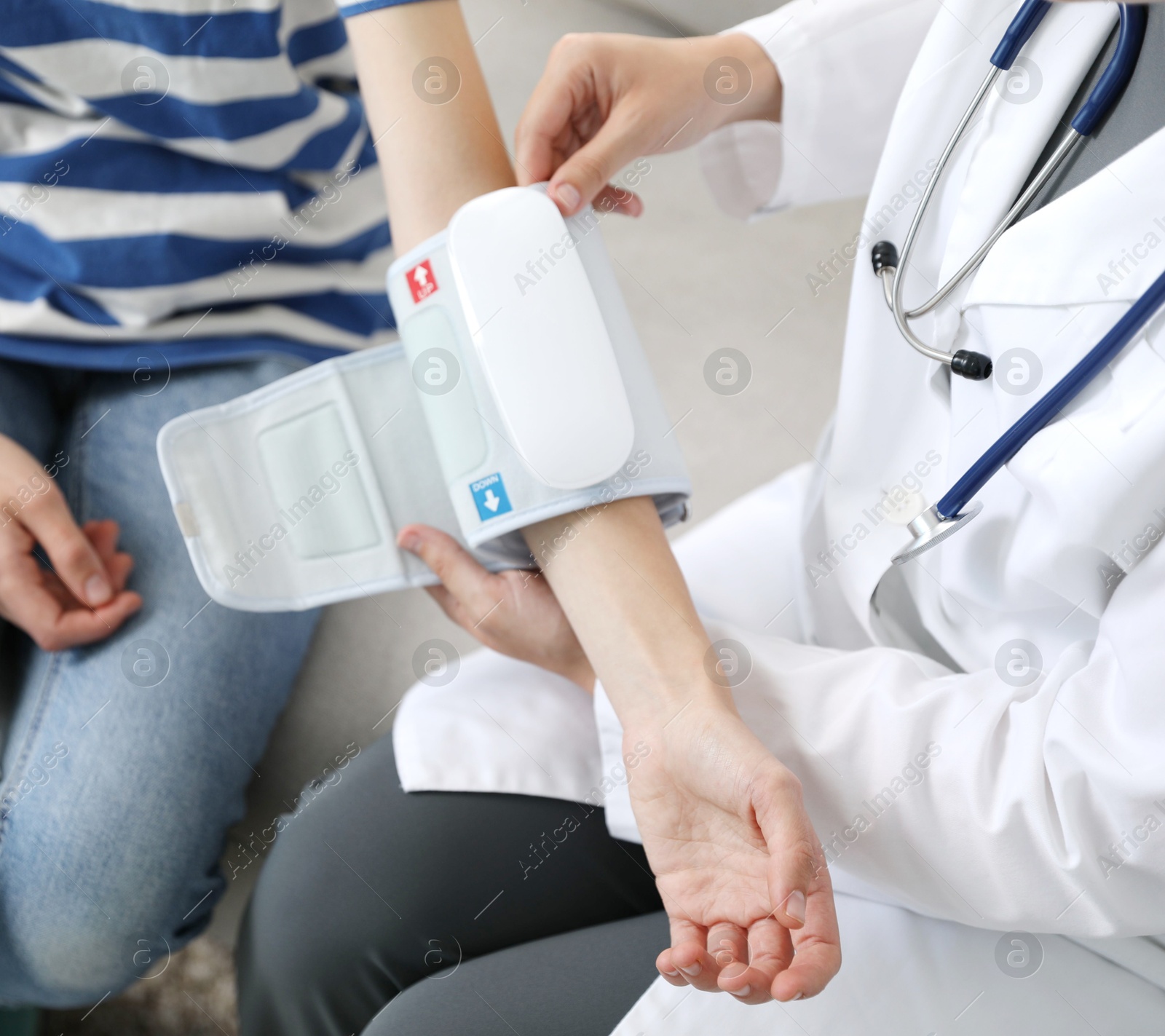 Doctor checking woman's heart rate and blood pressure via sphygmomanometer on sofa indoors, closeup Photo of Doctor checking woman's heart rate and blood pressure via sphygmomanometer on sofa indoors, closeup